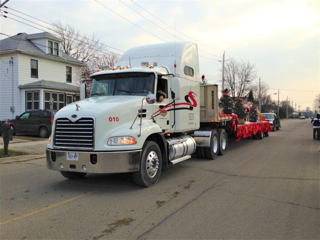 Truck pulling a flatbed with Christmas float set up on it.